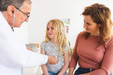 Kıdemli erkek doktor, annesinin yanında steteskopla küçük bir kızı muayene ediyor. Sağlık ve tıbbi konsept.