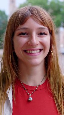 Şehrin caddesinde kameraya gülümseyen mutlu beyaz bir kızın dikey HD videosu. Şehir arka planında neşeli, güzel İtalyan kadın portresi.