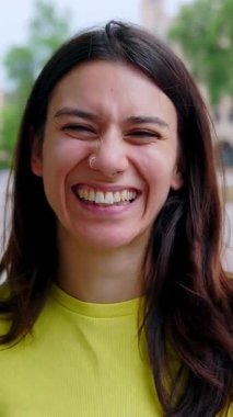 Şehrin caddesinde kameraya gülümseyen mutlu esmer kadının dikey HD videosu. Şehir arka planında neşeli, güzel İtalyan kadın portresi..