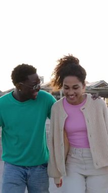 Açık havada kaynaşan neşeli genç arkadaş grubunun dikey HD videosu. Çok ırklı milenyum insanları birlikte vakit geçirip, şehrin sokaklarına gülüyorlar.