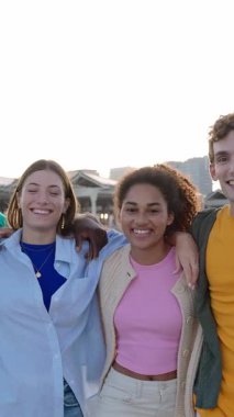 Birbirine sarılıp dışarıda kameraya gülümseyen çok ırklı genç bir arkadaş grubunun dikey HD videosu. Birlik, gençlik topluluğu ve arkadaşlık kavramı