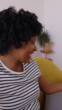 Mutlu Latin Amerikalı genç bir kadının, evdeki kanepede dinlenirken cep telefonu uygulamasını kullanarak en iyi arkadaşıyla görüntülü konuşması. O el sallıyor. İletişim yaşam tarzı konsepti. Dikey