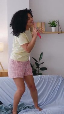 Evdeki pijama partisinde arkadaşlarıyla dans edip şarkı söyleyen mutlu Afrikalı Amerikalı kızın dikey HD videosu. Kadın arkadaşlığı kavramı