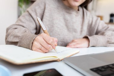 Evde dizüstü bilgisayardan öğrenirken not defterine notlar yazan kız öğrenci. Eğitim ve e-öğrenim kavramı