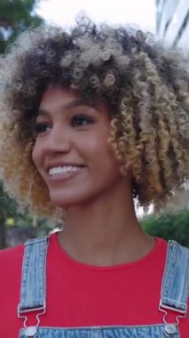 Kentin caddesinde afro saç stili gezen kendinden emin genç Latin Amerikalı kadının dikey HD ön görüntü videosu.