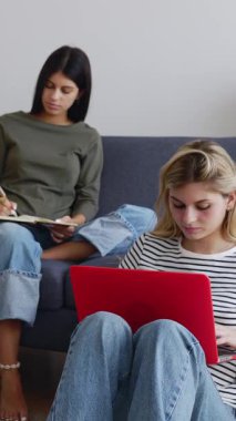 Oturma odasında birlikte çalışan iki genç kızın dikey HD videosu. Millennial bir grup kadın öğrenci aynı apartmanda üniversite atamaları üzerinde çalışıyor. Eğitim kavramı.