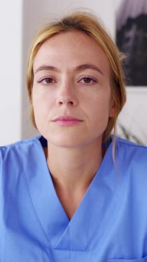 Dikey HD video. Genç kadın sağlık çalışanlarının POV 'u evden bir video görüşmesi yapıyor. Mavi önlüklü gülümseyen genç hemşire web konferansında hastaları dinliyor. Teletıp kavramı.