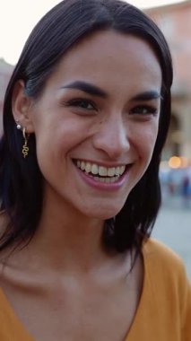 Şehrin caddesinde kameraya gülümseyen mutlu genç bir kadının dikey HD video portresi