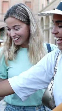 Haftalık giysi pazarında giysilere bakan üç genç kadının dikey HD videosu. Kadın turist alışveriş gününün tadını çıkarıyor. Açık hava pazarında ikinci el kıyafetlere bakıyor.
