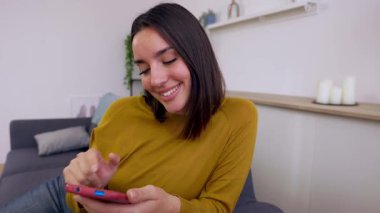 Kanepede cep telefonu kullanan mutlu genç bir kadın. Milenyum kadını evde dinleniyor cep telefonundan sosyal medya içeriğini kontrol ediyor. Teknoloji ve eğlence kavramı