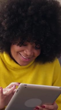 Kanepede oturmuş tablet bilgisayardaki medya içeriğini izlerken eğlenen mutlu Latin kadının dikey HD videosu. Teknoloji ve ev hayatı kavramı.