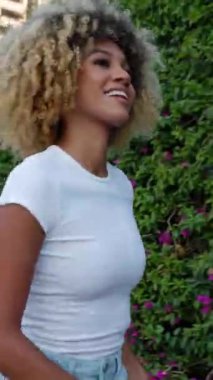 Şehir caddesinde dans ederken telefonla müzik dinleyen heyecanlı Latin Amerikalı kadının dikey HD videosu. Tasasız, kutlama ve mutluluk konsepti