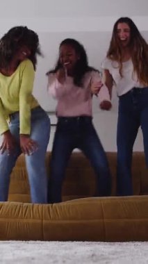 Evdeki kanepede dans eden, partiden keyif alan, birlikte kutlama yapan üç mutlu genç kızın dikey HD videosu.