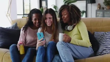 Three happy multiracial young women friends having fun using mobile phone. Multi-ethnic group of female student enjoying free time sharing funny pictures on social media app. Female friendship concept