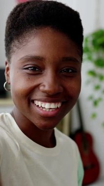 Mutlu, genç Afrikalı bir kadının evinde dinlenirken cep telefonu uygulamasını kullanarak bir video konuşması. Dikey HD video.