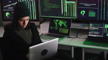 Arka planda birden fazla monitör olan karanlık odada siber saldırı için dizüstü bilgisayarda virüs kodları yazan profesyonel bir kadın hacker.