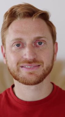 Yeni dairede otururken kameraya bakan mutlu kızıl adamın portresini yakın çekim. Mutlu insanlar, yeni hayat ve başlangıç konsepti. Dikey HD video.