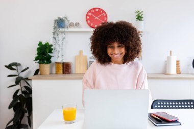 Genç mutlu Afro-Amerikan kadın mutfak masasında dizüstü bilgisayar kullanıyor. Ev ve iş konseptinden çalışmak