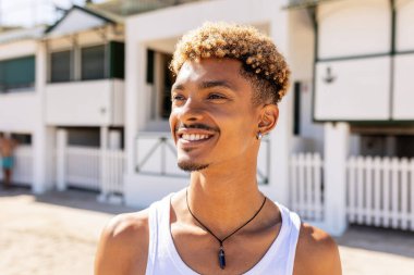 Kaygısız genç adam gülümsüyor ve sahildeki evlerin yanında tatilin tadını çıkarıyor. Mutluluk ve rahatlığı ifade ediyor.