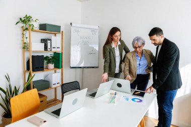 Modern ofis ortamında bir proje üzerinde iş birliği yapan iş ekibi, dizüstü bilgisayarlar ve iş planlı bir beyaz tahta kullanıyor. İş konsepti