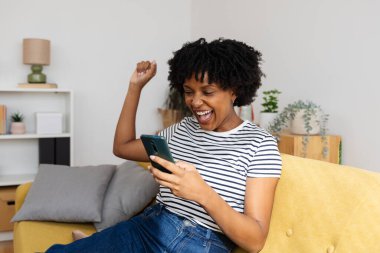 Genç Afrikalı Amerikalı kadın telefonuyla iyi haberi kutluyor, ihbarla olumlu mesaj ya da başarı alıyor