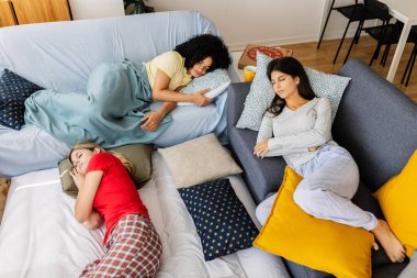 Genç kadınlar rahat bir kanepe ve yerde dinleniyor, evde pijama partisinin tadını çıkarıyor, yastıklar ve kahkahalarla çevrili. Kadın arkadaşlığı ve gençlik kavramı
