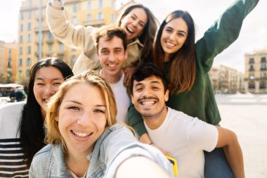 Çeşitli gençler tatil sırasında şehir caddesinde eğleniyorlar. Bir grup neşeli çoklu etnik arkadaş dışarıda selfie çekiyor. Gençlik toplumu ve arkadaşlık kavramı