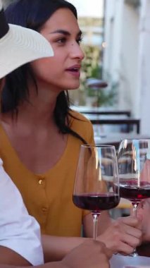 Kırmızı şarapla aperatifin tadını çıkaran üç mutlu kadının barın dışındaki masada otururken çekilmiş dikey HD videosu. Yiyecek ve içecek konsepti.