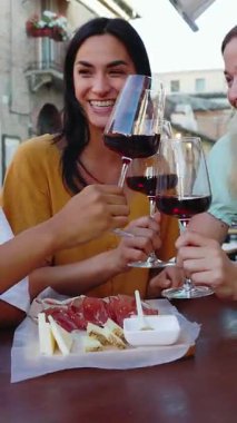 Yaz tatilinde restoranın masasında oturmuş kırmızı şarap içen üç genç kadının dikey HD videosu. Kadın arkadaşlığı ve tatil yaşam tarzı konsepti.