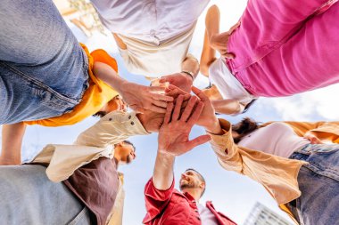 Eller üst üste yığılmış çok ırklı mutlu arkadaşlar. Çok ırklı çeşitli üniversite öğrencileri ellerini birleştiriyor. El konsepti, topluluk, birlik ve takım çalışması yığılıyor. Düşük açı görünümü