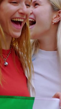 İtalyan bayrağını açık havada tutarken çığlık atan ve kutlama yapan çeşitli genç kadınların dikey HD videosu. Farklı milletlerden İtalyan vatandaşlar birlik gösteriyor.