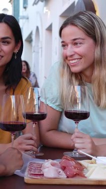 Restoranda kırmızı şarapla aperatiften keyif alan üç genç kadının dikey HD videosu. Kadın arkadaşlığı ve tatil yaşam tarzı konsepti.