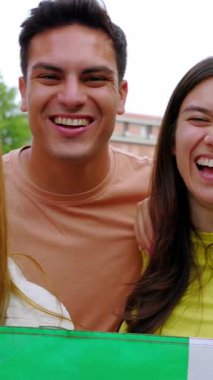İtalyan bayrağını açık havada tutarken kameraya gülümseyen çeşitli gençlerin dikey HD videosu. Farklı milletlerden İtalyan vatandaşları birlik gösteriyor