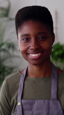 Neşeli, gülümseyen bir bayan küçük işletme sahibinin portresi. Genç siyahi girişimci kadın fabrika atölyesinde duruyor. Dikey görüntüler.