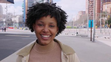 Şehir sokağında kameraya gülümseyen mutlu Afrikalı genç Amerikalı kız. Şehir arka planında neşeli, güzel siyahi kadın portresi