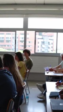 Üniversitede ya da okulda öğretmenlik yapan yetişkin bir kadının dikey HD videosu. Bayan öğretmen sınıftaki öğrencilerine bir ders veriyor. Lise ve ortaöğretim