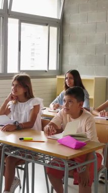 Bir grup ilkokul öğrencisinin öğretmenlerin sorularını cevaplamak için el kaldırdığı dikey HD videolar. Eğitim yaşam tarzı kavramı