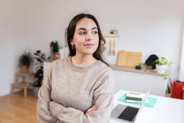 Evde internetten öğrenme molası verirken dizüstü bilgisayarlı genç bir bayan mutfakta duruyor.