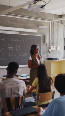 Yetişkin öğretmenleri dinleyen lise öğrencilerinin dikey HD videosu tahtaya yazılmış kimya formüllerini anlatıyor. Eğitim yaşam tarzı kavramı