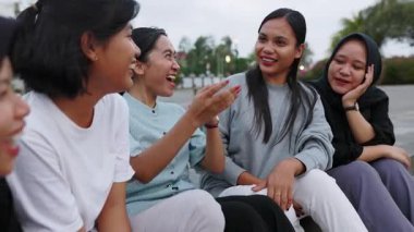 Endonezyalı genç bir grup kadın şehir caddesinde rahatça takılıyor. Gen Z Asyalı öğrenci arkadaşları birlikte otururken gülüyorlar. Kadın arkadaşlığı ve gençlik toplumu kavramı.