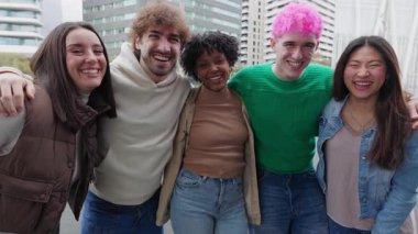 Çok ırklı genç arkadaşların portresi. Birbirlerine sarılıyorlar. Dışarıda kameraya gülümsüyorlar. Gençlik toplumu ve uluslararası arkadaşlık kavramı