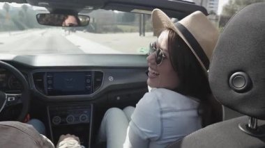 Cabriolet yolculuğunda gülen mutlu genç çift. Şehirde kiralık araba sürerken erkek arkadaşına bakan, yaz şapkalı bir kadın. Tatil ve seyahat kavramı