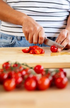 Dikey çekimde tanınmayan kadın elleri ahşap kesme tahtasıyla domates doğruyor, mutfakta sağlıklı salata hazırlıyor.