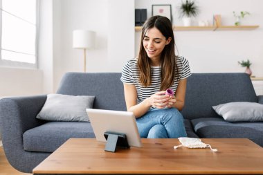 Elinde regl fincanı olan genç bir kadın evdeki dijital tablete bakarak talimatları kullanıyor. Kadın hijyenik yaşam tarzı ve bin yıllık insan üretim kavramı