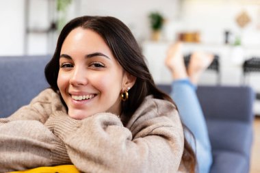 Huzurlu genç bir kadın oturma odasında rahat bir kanepede uzanıp huzur ve mutluluğun tadını çıkarıyor.