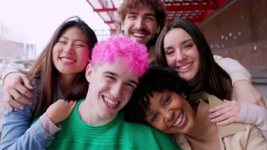 Caddede kameraya gülümseyen çeşitli genç insanların toplu portresi. Gençlik toplumu kavramı, çok ırklı arkadaşlarla kentsel arka planda birbirlerine sarılıyorlar. Arkadaşlık ve çeşitlilik kavramı.