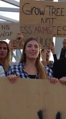 Dünyadaki savaş ve şiddeti protesto eden posterler ve pankartlar taşıyan çok ırklı aktivistlerin dikey HD videosu.