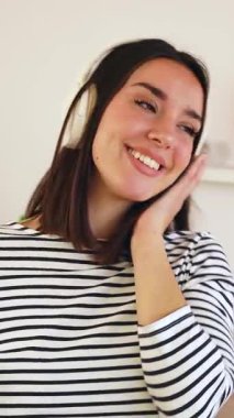 Kırmızı şarap içen, internetten müzik dinleyen, kablosuz kulaklıklı ve evde şarkı söyleyen mutlu bir kadının dikey HD videosu.