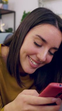 Kanepede uzanan telefon uygulaması üzerinden internetten ödeme yapan genç bir kadının dikey HD videosu. Milenyum güzeli kadın internetten alışveriş yapıyor evden uzaktan ödeme yapıyor..