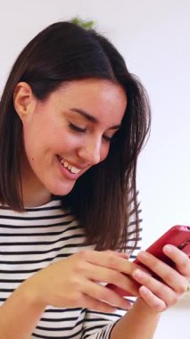 Genç mutlu bir kadının evdeki mutfakta cep telefonu kullanıp uygulamadan sosyal medya içeriğini izlerken eğlendiği dikey HD videolar. Teknoloji ve ev hayatı kavramı